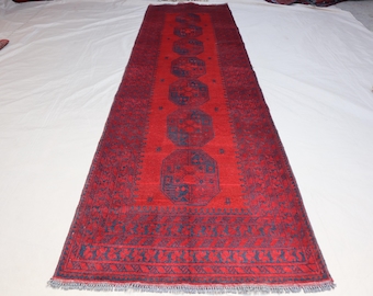 May include: A red and blue runner rug with a traditional Persian design. The rug has a geometric pattern with a central medallion and a border.