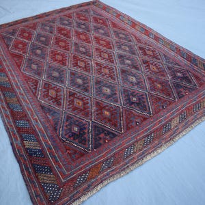 May include: A rectangular, hand-woven rug with a geometric diamond pattern in shades of red, blue, and brown. The rug has a detailed border with various patterns and colors. The rug is likely made of wool and is suitable for a living room or bedroom.