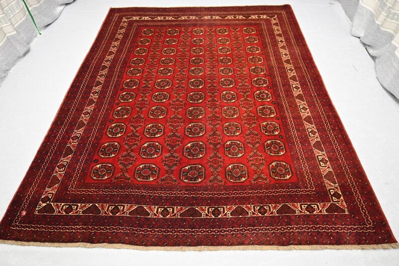 May include: A rectangular, red oriental rug with a detailed geometric pattern. The rug features a central field of repeating medallions and a border with intricate designs. The color palette includes shades of red, brown, and cream.