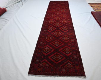 Op de afbeelding: Een lange, rechthoekige loper met een dieprood en donkerbordeaux kleurenpalet. Het oppervlak is versierd met een herhalend patroon van grote, onderling verbonden ruiten met daarin ingewikkelde geometrische motieven en kleine sterren.