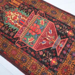 Könnte beinhalten: Ein traditioneller türkischer Teppich mit schwarzem Hintergrund und komplizierten floralen Mustern in Rot-, Orange-, Grün- und Blautönen. Der Teppich zeigt ein zentrales Design einer Vase mit Blumen und Blättern.