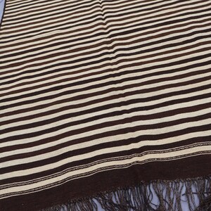 May include: A brown and white striped woven rug with fringe. The rug has a simple design with alternating brown and white stripes.
