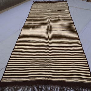 May include: A long, striped rug with brown and white stripes. The rug has a fringe on both ends.
