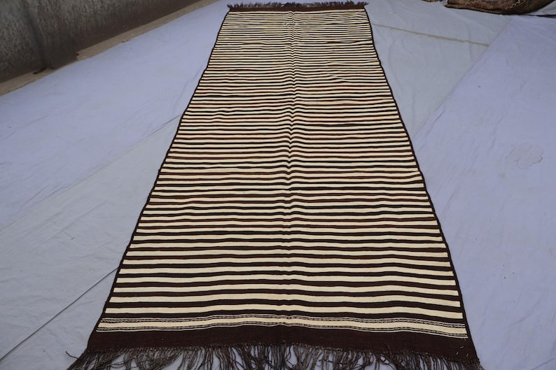 May include: A long, striped rug with brown and white stripes. The rug has a fringe on both ends.