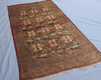 Könnte beinhalten: Rechteckiger Teppich mit detailliertem Muster in Braun-, Beige- und Grüntönen. Der Teppich weist ein zentrales Design mit sich wiederholenden floralen und geometrischen Motiven auf, das von einem Rand mit komplizierten Mustern umrahmt wird. Der Teppich hat einen Fransenrand.