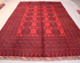 May include: A large, rectangular red rug with a detailed black geometric pattern. The rug features a central field of repeating octagonal shapes and intricate border designs. The rug is displayed on a white surface.