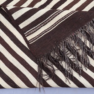 May include: A brown and white striped woven rug with fringe. The rug has a diagonal pattern and is made of a soft, textured material.