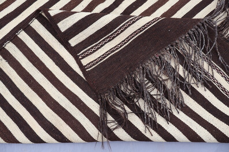 May include: A brown and white striped woven rug with fringe. The rug has a diagonal pattern and is made of a soft, textured material.