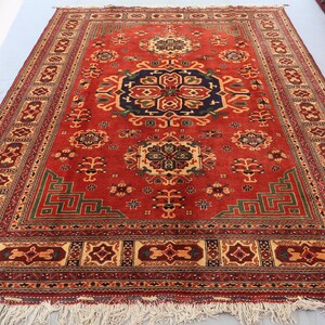 May include: A red oriental rug with a central navy blue medallion and detailed geometric patterns. The rug has a decorative border and fringe, with measurements in centimetres.