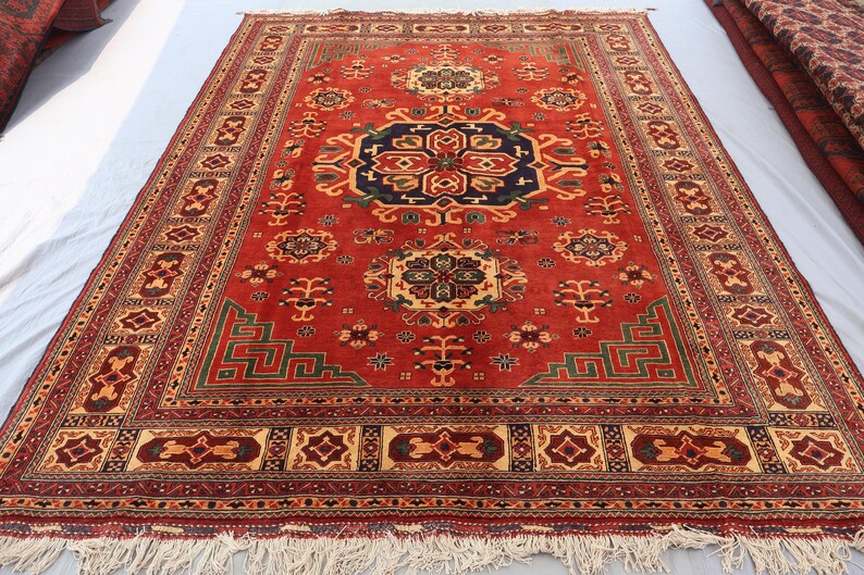 May include: A red oriental rug with a central navy blue medallion and detailed geometric patterns. The rug has a decorative border and fringe, with measurements in centimetres.