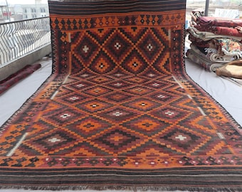 May include: A large, rectangular rug with a geometric diamond pattern in shades of orange, brown, and black. The rug has a fringed edge and is displayed outdoors. The design features repeating diamond shapes with white accents.