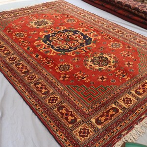 May include: A red oriental rug with a central medallion design and a detailed border. The rug has intricate geometric patterns in blue, green, and gold. The rug has a fringed edge.