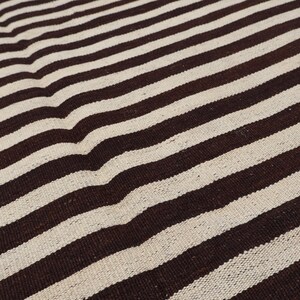 May include: A close-up of a brown and white striped fabric. The fabric has a woven texture and is made of natural fibers.
