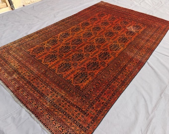 May include: A rectangular area rug featuring a deep red and black colour palette. The central field displays a repeating geometric pattern of dark medallions, surrounded by a wide, intricate border with floral and linear motifs and fringe.
