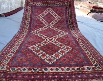 Puede incluir: Una alfombra persa tradicional con un patrón geométrico rojo, azul y blanco. La alfombra tiene un diseño en forma de diamante en el centro y un borde con un patrón de estrella repetido.