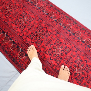 May include: A red runner rug with a traditional Persian design. The rug has a black and gold border and intricate floral patterns.
