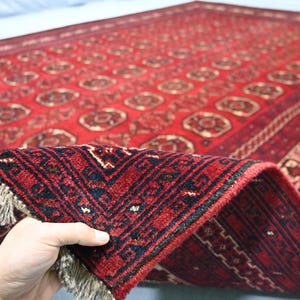 May include: A red and black patterned rug with a detailed design. The rug is folded to show the underside, revealing a fringe. The rug's pattern includes repeating floral motifs and geometric borders. The rug is likely made of wool.