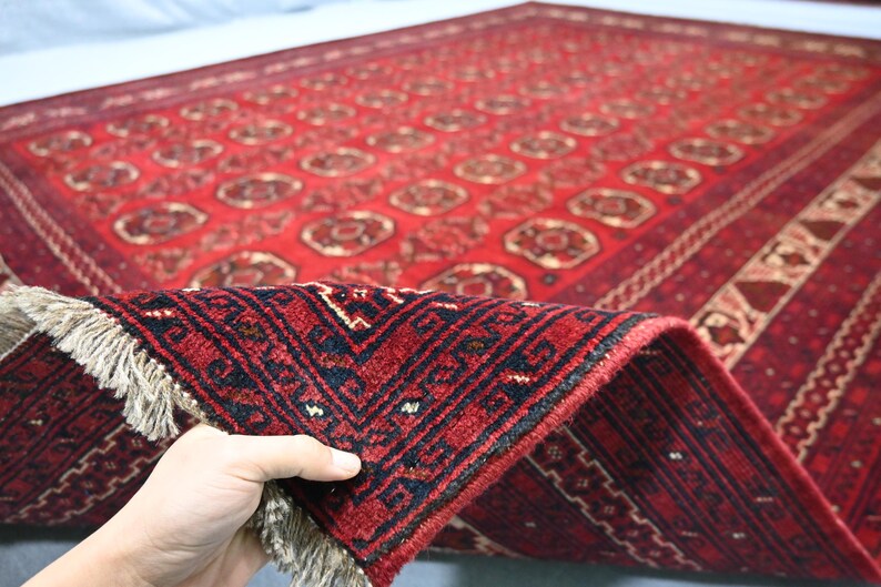 May include: A red and black patterned rug with a detailed design. The rug is folded to show the underside, revealing a fringe. The rug's pattern includes repeating floral motifs and geometric borders. The rug is likely made of wool.