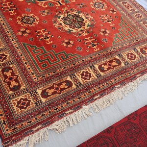 May include: A vibrant red oriental rug with a central medallion and detailed border patterns. The rug displays geometric designs in green, beige, and burgundy, with a fringed edge. The rug is likely made of wool.