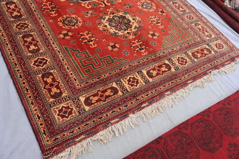 May include: A vibrant red oriental rug with a central medallion and detailed border patterns. The rug displays geometric designs in green, beige, and burgundy, with a fringed edge. The rug is likely made of wool.