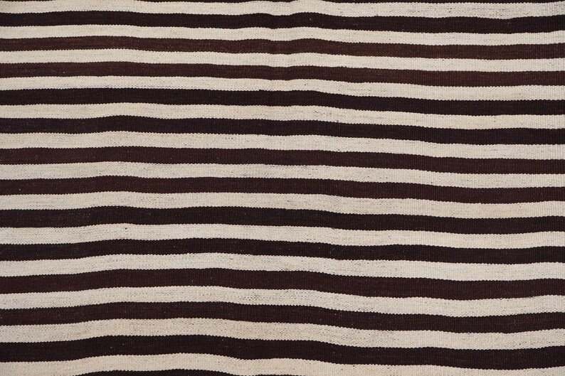 May include: A close-up of a striped fabric with alternating brown and white stripes. The fabric is woven and has a slightly textured surface.