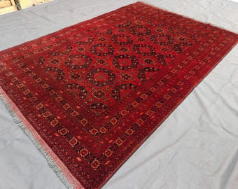 May include: A rectangular area rug featuring a deep red background with a repeating pattern of black geometric octagonal motifs. The rug includes a detailed border with floral-like shapes and ends with short, light-colored fringe on both sides.