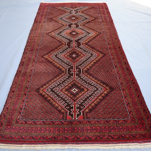 May include: A traditional Persian rug with a red, brown, and cream color scheme. The rug features a geometric pattern with intricate details. The rug has a fringe border.