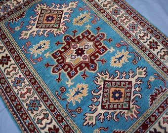 May include: A blue rug with a traditional Persian design. The rug has a central medallion with intricate floral patterns and a border with geometric motifs. The colors are vibrant and include shades of blue, red, yellow, and white.