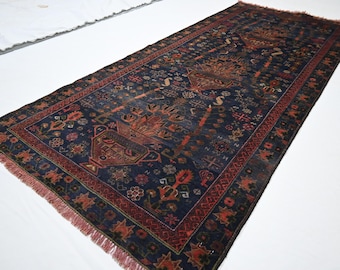Puede incluir: Una alfombra rectangular que presenta un campo azul marino profundo con intrincados patrones florales y geométricos en tonos rojo, naranja y crema. La alfombra tiene un borde decorativo ancho y flecos cortos en ambos extremos.