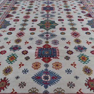 May include: A large, off-white rug with a repeating pattern of colorful geometric shapes. The design includes red, blue, green, and yellow elements, with a detailed border. The rug's design is symmetrical and covers the entire surface.