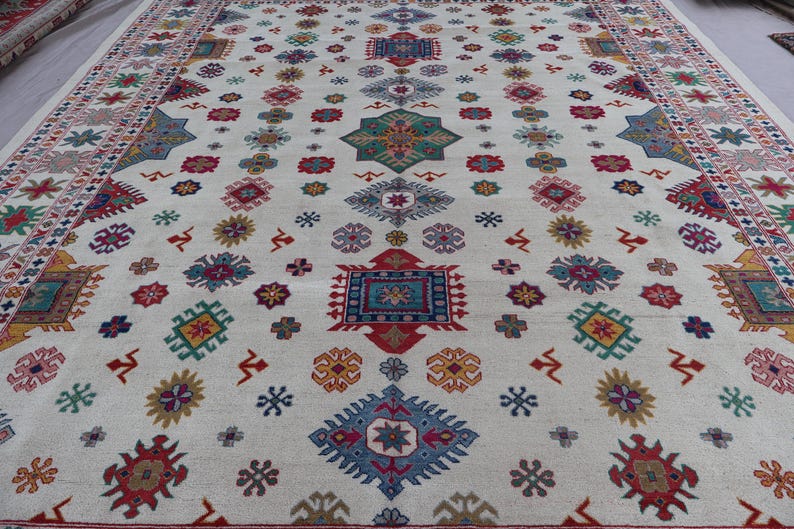 May include: A large, off-white rug with a repeating pattern of colorful geometric shapes. The design includes red, blue, green, and yellow elements, with a detailed border. The rug's design is symmetrical and covers the entire surface.