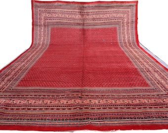May include: A large, rectangular red rug with an intricate pattern. The rug features a central field of small, repeating motifs, framed by multiple borders with detailed designs in shades of beige, brown, and blue. The rug is displayed on a white background.