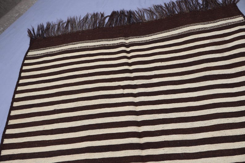 May include: A brown and white striped rug with fringe on all sides.