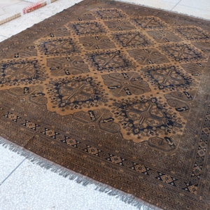 May include: A rectangular area rug featuring a repeating diamond pattern in dark brown and black tones. The central field displays intricate geometric motifs within each diamond, framed by a wide, detailed border with fringe on the short ends.