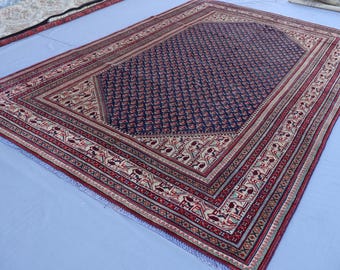 May include: A traditional Persian rug with a navy blue center and intricate red, white, and cream border patterns.