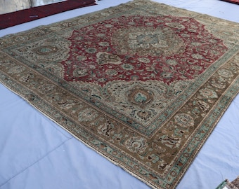 May include: A vintage rug with a red, green, and brown floral pattern. The rug has a faded, worn look, giving it a unique antique aesthetic.