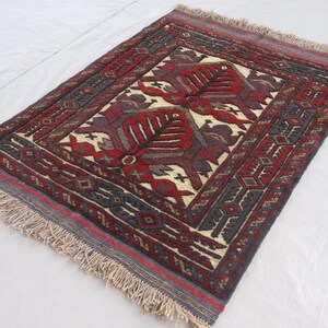 Puede incluir: Alfombra rectangular con un diseño floral central en rojo, crema y burdeos. La alfombra tiene un borde oscuro con patrones geométricos y bordes con flecos. La alfombra probablemente está anudada a mano y es adecuada para una sala de estar o un dormitorio.