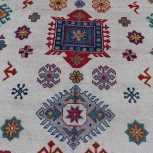 May include: A cream-colored rug with a repeating pattern of colorful geometric shapes. The design includes squares, diamonds, and floral motifs in shades of red, blue, yellow, and green. The rug has a textured surface.