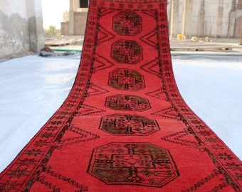 Puede incluir: Una alfombra de pasillo roja con un patrón geométrico en negro y marrón. La alfombra tiene un diseño tradicional con motivos repetidos.