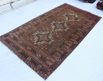 May include: A rectangular area rug featuring a dark brown field with three central geometric medallions in cream and muted tones. The rug has a wide, intricate border with repeating patterns and short fringe along the edges of the woven textile.