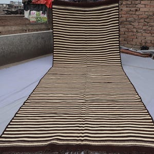 May include: A long, striped rug with brown and white stripes. The rug has a fringe on the ends.
