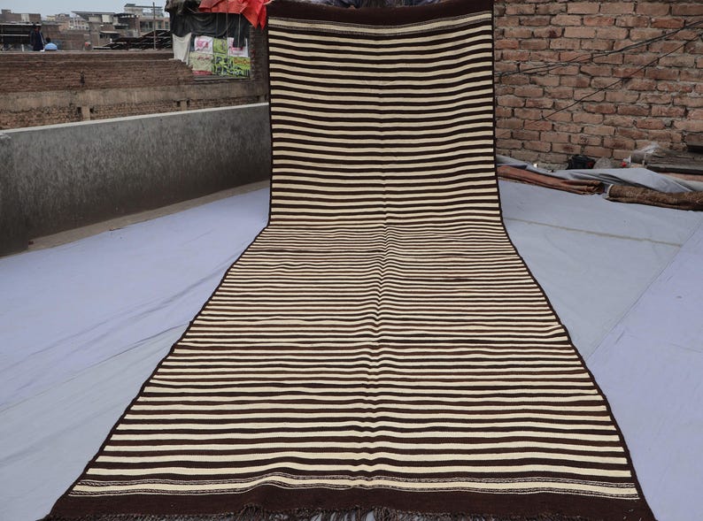 May include: A long, striped rug with brown and white stripes. The rug has a fringe on the ends.