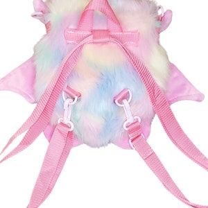 Może przedstawiać: R&oacute;żowy pluszowy plecak w tęczowych kolorach z regulowanymi szelkami. Plecak ma puszystą fakturę i kształt małego zwierzęcia.