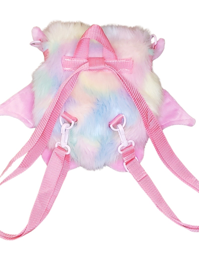 Może przedstawiać: R&oacute;żowy pluszowy plecak w tęczowych kolorach z regulowanymi szelkami. Plecak ma puszystą fakturę i kształt małego zwierzęcia.
