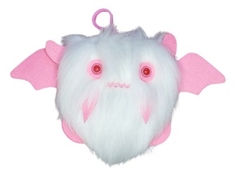 May include: A white fluffy plush bat with pink wings and red eyes. The bat has a pink mouth and a loop on top of its head.