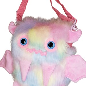Może przedstawiać: R&oacute;żowa i tęczowa pluszowa torba na ramię w kształcie potwora z dużymi niebieskimi oczami i r&oacute;żowym paskiem.