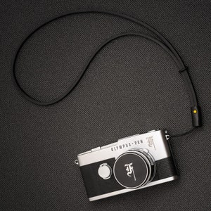 May include: A silver Olympus Pen camera with a black leather strap. The camera has a black and white design with the text "OLYMPUS PEN" and a black "F" logo.