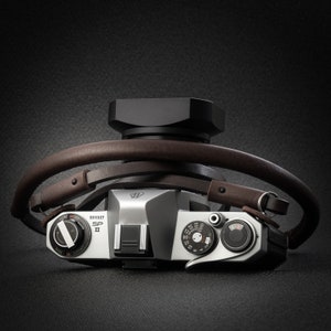 May include: A silver camera with a brown leather strap. The camera has a lens cap on top and the text "SP II" and "6911327" on the front.