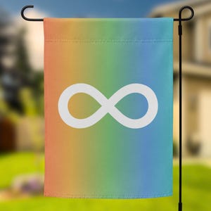 May include: A garden flag with a rainbow gradient background and a white infinity symbol. The flag is hanging on a black metal pole in front of a house and green grass.