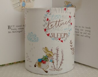 May include: White fabric lampshade with a Peter Rabbit design. The lampshade features a quote: "Eating too much lettuce makes me sleepy."